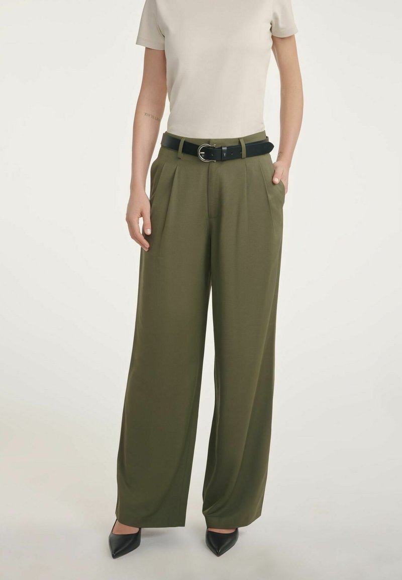 Oliwkowe spodnie z szerokimi nogawkami i wysokim stanem, z eleganckimi plisami i dwiema kieszeniami, zestawione z czarnym paskiem i dopasowaną beżową bluzką.