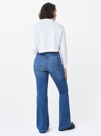 Camicia bianca a maniche lunghe cropped abbinata a jeans blu a zampa d'elefante. I jeans presentano tasche posteriori e una leggera scoloritura. Scarpe con plateau nere completano il look.