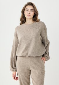 Top en tricot texturé beige à manches longues et col rond, assorti à un pantalon texturé. Les deux pièces présentent une coupe décontractée.