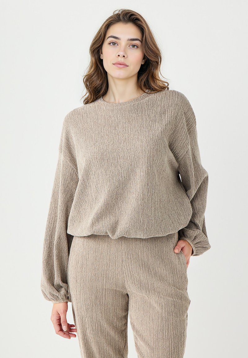 Top en tricot texturé beige à manches longues et col rond, assorti à un pantalon texturé. Les deux pièces présentent une coupe décontractée.