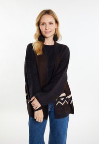 Cardigan supradimensionat de culoare brun închis, confecționat dintr-un tricot moale, cu modele geometrice în alb și bej. Dispune de mâneci late și un design deschis în față.