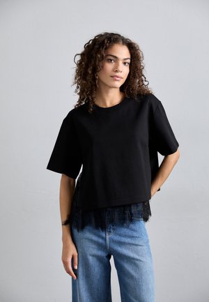 Must beebi lühikeste varrukatega ja pitsäärisega must cropped t-särk, millele sobivad helesinised laiad teksad. Sile kangatekstuur.