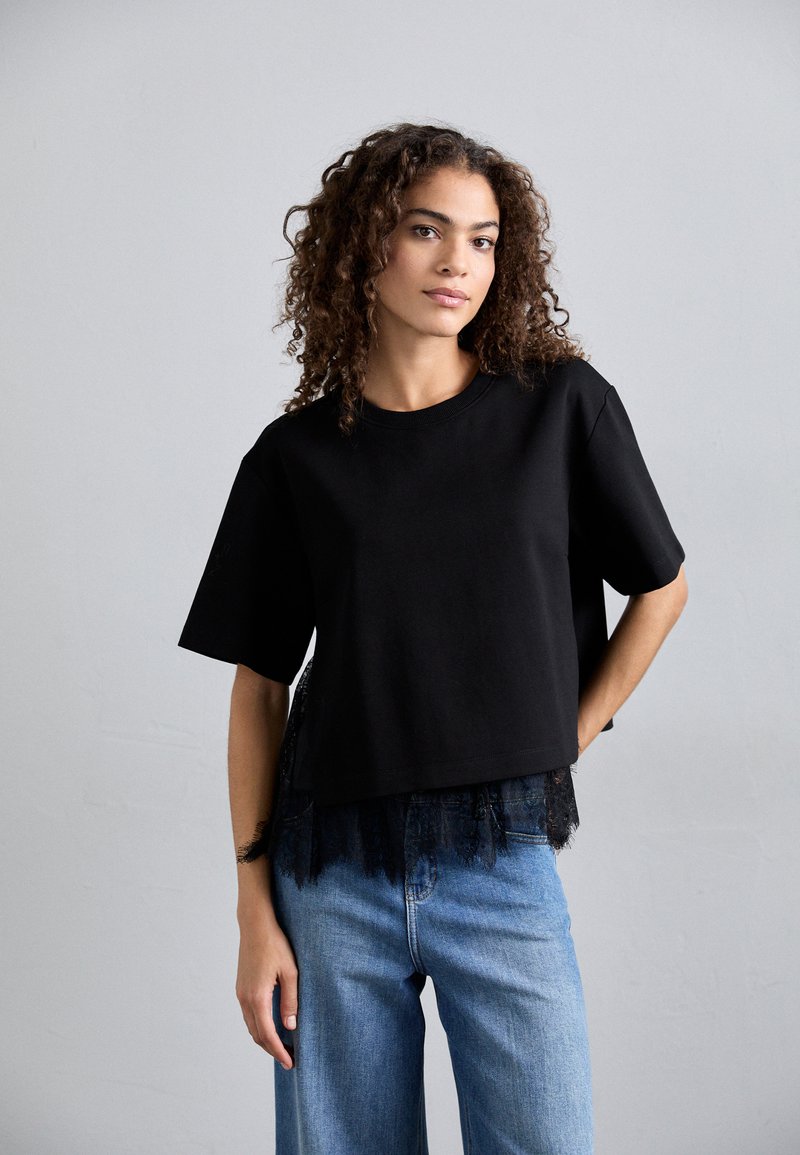 Czarny krótki t-shirt z krótkim rękawem i koronkowym wykończeniem na dole, zestawiony z jasnoniebieskimi spodniami typu wide-leg. Gładka faktura materiału.