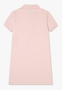 Vaaleanpunainen lyhythihainen polo-mekko, jossa on ribbikuvioinen kauluskanta ja hihansuut, näkyy takaa yksinkertaisella valkoisella taustalla.