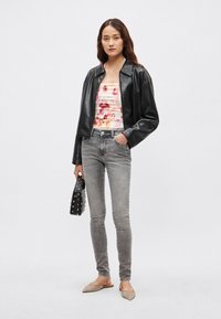 Czarna krótka kurtka ze skóry na kwiecistej, wielokolorowej koszulce na ramiączkach. Szare obcisłe dżinsy, beżowe zdobione baleriny i czarna kopertówka z ćwiekami.