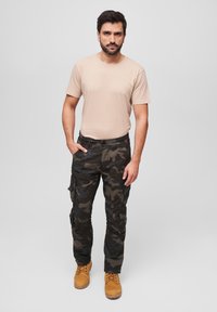 Beige t-shirt, camouflage cargo pants with pockets, and brown boots. Pants feature a relaxed fit, durable fabric, and a variety of tones.