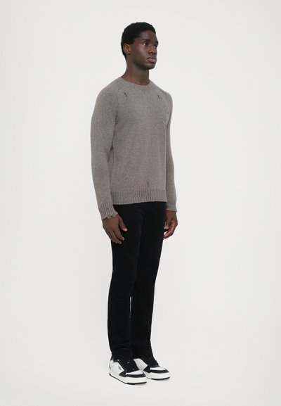 Pull en tricot gris clair, avec un col rond et des poignets côtelés. Associé à un jean noir slim et des baskets noir et blanc.