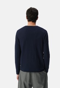 Granatowa koszula z długim rękawem, uszyta z miękkiego materiału, z okrągłym dekoltem i luźnym krojem, w połączeniu z jasnoszarymi spodniami.