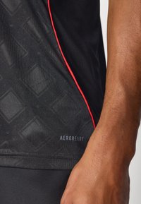 Juoda sportinė marškinėliai su deimanto raštu, raudonais akcentais siūlėse ir "AEROREADY" užrašu prie apačios, išryškinančiu drėgmę atstumiant technologiją.