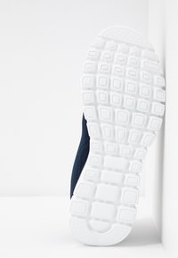 Idrettssko med et strukturert navy mesh-overdel og en tykk hvit gummisåle med rektangulære mønstre for grep.