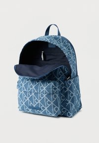 Μπλε τζιν σακίδιο με γεωμετρικό λευκό μοτίβο, μεγάλο κύριο χώρο, καπάκι με πτερύγιο, εμπρόσθια τσέπη και εσωτερική τσέπη με φερμουάρ.