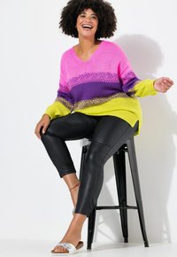 Maglione oversize a V con righe rosa, viola e verde lime. I leggings in faux pelle neri e i sandali metallici flat completano il look.