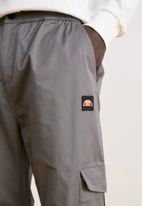 Grå cargo bukser lavet af tekstureret stof, med elastisk talje, sidelommer og et lille farverigt logo-patch på låret.