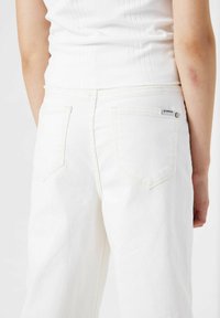 Jeans de mezclilla blanca con una cintura alta, diseño de cinco bolsillos, bolsillos traseros con costura y una pequeña etiqueta de la marca en el bolsillo trasero derecho.
