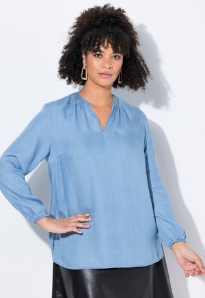 Lichtblauwe blouse met lange mouwen, een V-hals en geplooide details bij de schouders. Glad materiaal en een comfortabele pasvorm. Zoom op taillehoogte.