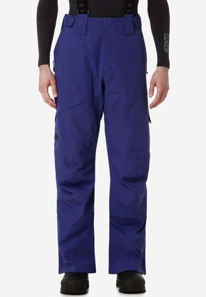 Pantaloni da sci impermeabili blu con bretelle indossati da una persona con stivali neri e una maglia nera a maniche lunghe con scritto "4CENTO" sulla manica.