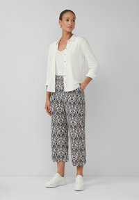 Biały kardigan zapinany na guziki noszony na kremowym topie bez rękawów, w połączeniu z wzorzystymi granatowo-białymi spodniami szerokimi i białymi trampkami, z podwiniętymi rękawami.