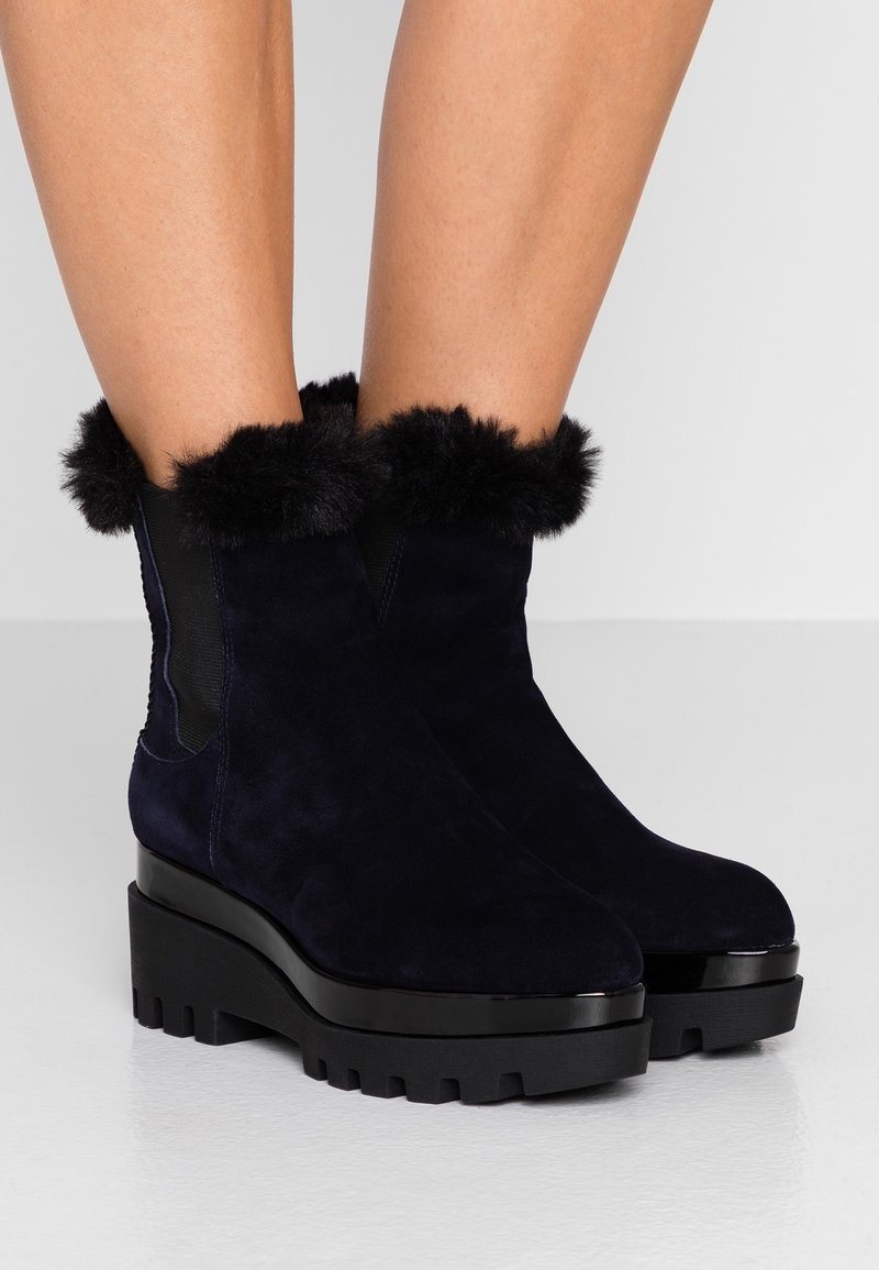 Granatowe zamszowe botki za kostkę z czarną sztuczną futrzaną lamówką przy mankiecie, masywną czarną podeszwą na platformie o żłobionej fakturze oraz elastycznymi panelami po bokach.