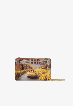 Borsa clutch gialla convertibile che percorre una strada fiancheggiata da fiori gialli verso il Colosseo a Roma, con tracolla a catena dorata.