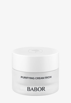 Pot de crème blanc opaque avec une finition brillante, un fond transparent et un couvercle plat blanc. Le texte sur le pot indique "Crème Purifiante Riche" et "BABOR."