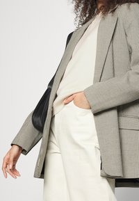 Blazer i rutigt tyg, ljusgrått och svart, med en skräddarsydd passform, djupa fickor och en slät svart satinaccent.