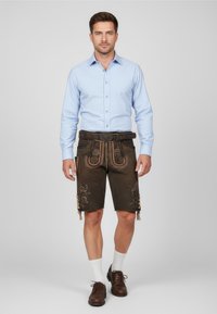 Brown lederhosen shorts with decorative stitching and patterns, paired with a light blue button-up shirt and brown shoes, worn with white socks.