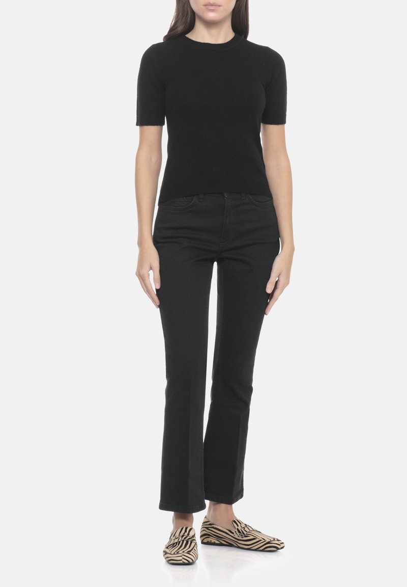 Maglietta nera a maniche corte in maglia abbinata a jeans neri aderenti e scarpe slip-on con motivo a zebre. Texture liscia e silhouette aderente.