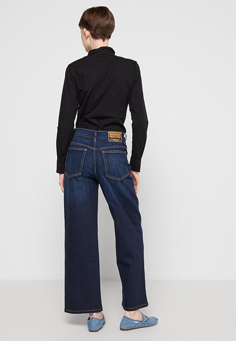 Jeans in denim a gamba larga di colore blu scuro, caratterizzati da un classico design a cinque tasche e da un'etichetta in pelle sulla vita posteriore.