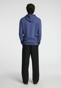 Felpa blu con un design sul retro, dotata di tasca a marsupio e cappuccio regolabile con cordino, abbinata a pantaloni neri a gamba larga.