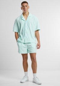 Conjunto de dos piezas en verde menta claro que incluye una camisa de botones de manga corta y pantalones cortos a juego. Tejido texturizado con un discreto detalle de patrón.