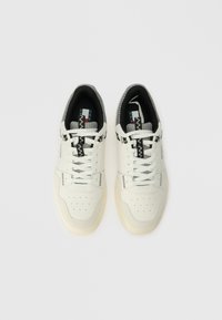 Sneakers brancos feitos de couro e tecido, com detalhes em preto e cinza com padrão, bico redondo e design de atar com perfurações.