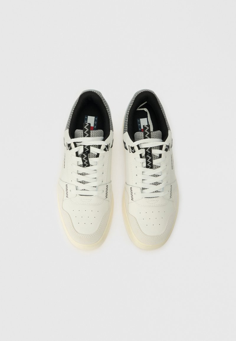 White sneakers made of leather and fabric, featuring black and gray patterned accents, round toe, and lace-up design with perforations.