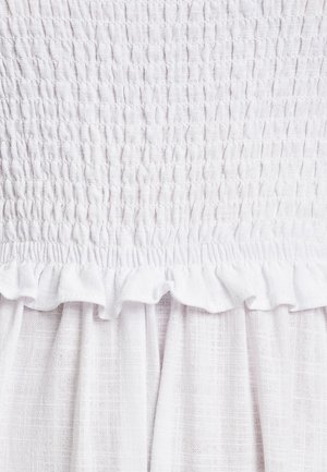 Robe blanche avec un corsage froncé et un motif texturé, et un ourlet volanté en tissu léger.