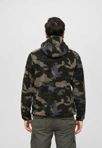Fleece hoodie in a camouflage pattern of dark greens, grey, and black. Features a hood and textured, fluffy fabric.