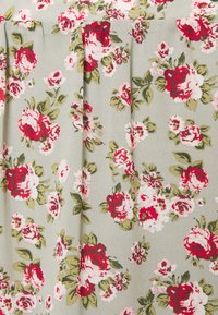 Beiger Stoff mit einem floralem Muster aus roten, rosa und weißen Rosen sowie grünen Blättern, mit vertikalen Falten.