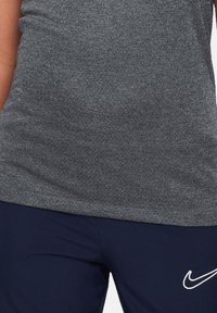 Graues sportliches tank-top mit weicher textur, kombiniert mit navy-blauen hosen, die ein weißes Nike-logo haben. Einfaches design, leistungsorientierte materialien.
