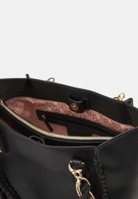 Sac à main en cuir noir avec ferrures dorées, présentant un extérieur texturé, une doublure rose à motifs et plusieurs compartiments intérieurs.