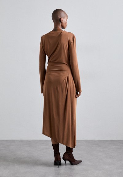 Vestido largo marrón de manga larga con un corte relajado y detalle de espalda drapeada, hecho de una tela suave. Combinado con botines marrones de tobillo con punta afilada.