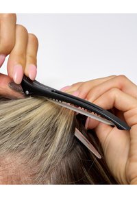 Svart hårklämma placerad över blonda och bruna hårstrån, som visar en texturerad yta, smal design och fina tänder för grepp.