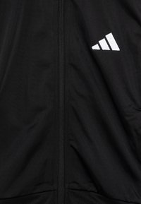 Juodas užtrauktuku užsegamas džemperis, pagamintas iš lygaus audinio; turi baltą Adidas logotipą; minimalistinis dizainas, be papildomų raštų ar detalių.
