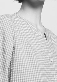 Grå och vit rutig skjorta med rundad krage, korta ärmar och fem matchande knappar fram. Texturerad bomullstyg.