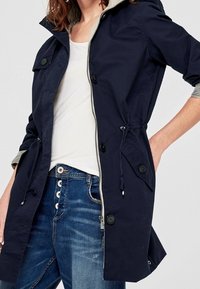 Navy blue lightweight jacket with a hood, elastic waist, and snap buttons. Features grey lining and an A-line cut for added comfort.
