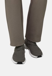 Chaussures de sport grises avec dessus en mesh texturé et semelles blanches, associées à un pantalon de survêtement gris fuselé. Ourlet plat aux jambes du pantalon.