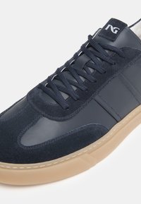 Sneaker in pelle e camoscio blu navy con pannelli laterali texturizzati, lacci piatti e una suola in gomma beige. Presenta il logo sulla linguetta.