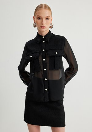 Black button-up shirt with a textured, frayed upper layer; transparent sleeves; two chest pockets; pearl buttons; paired with a matching skirt.