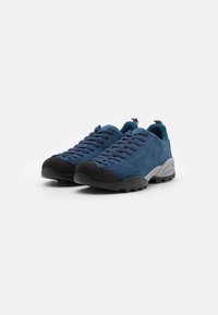 Niebieskie zamszowe buty z czarnym gumowym czubkiem i teksturowaną szaro-skalną podeszwą. Posiadają sznurowany design, z siateczkowym wyłożeniem i pętelką na pięcie.