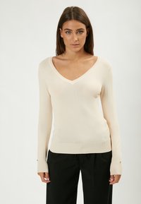 Maglione beige a maniche lunghe con scollatura a v, realizzato in materiale morbido; polsini a costine con dettagli in bottone; texture liscia; design aderente.