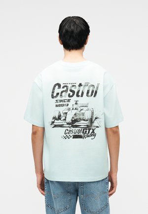 Άτομο που φοράει ανοιχτό μπλε μπλουζάκι με μαύρο γραφικό αγωνιστικού αυτοκινήτου και το κείμενο «Castrol GTX Racing» στην πλάτη.