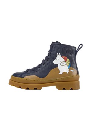 Marineblauwe en beige leren veterlaars met dikke zool, met aan de zijkant een wit cartoonfiguurtje dat kleurrijke opgerolde tassen draagt.