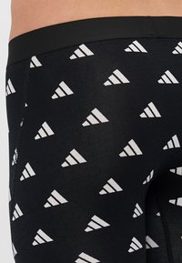 Fekete leggings sima textúrával, amelyen ismétlődő fehér háromszög minta található. A derékpánt fekete és rugalmas.